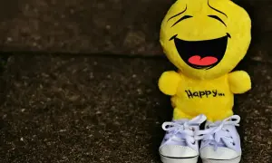 Żółta maskotka z napisem "Happy..." i śmiesznymi cytatami na twarzy, w białych trampkach.