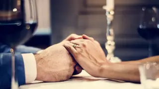 Dłonie splecione na stole, pierścionek na palcu, świeca i kieliszki wina. Idealne wzruszające życzenia na rocznicę ślubu dla męża.