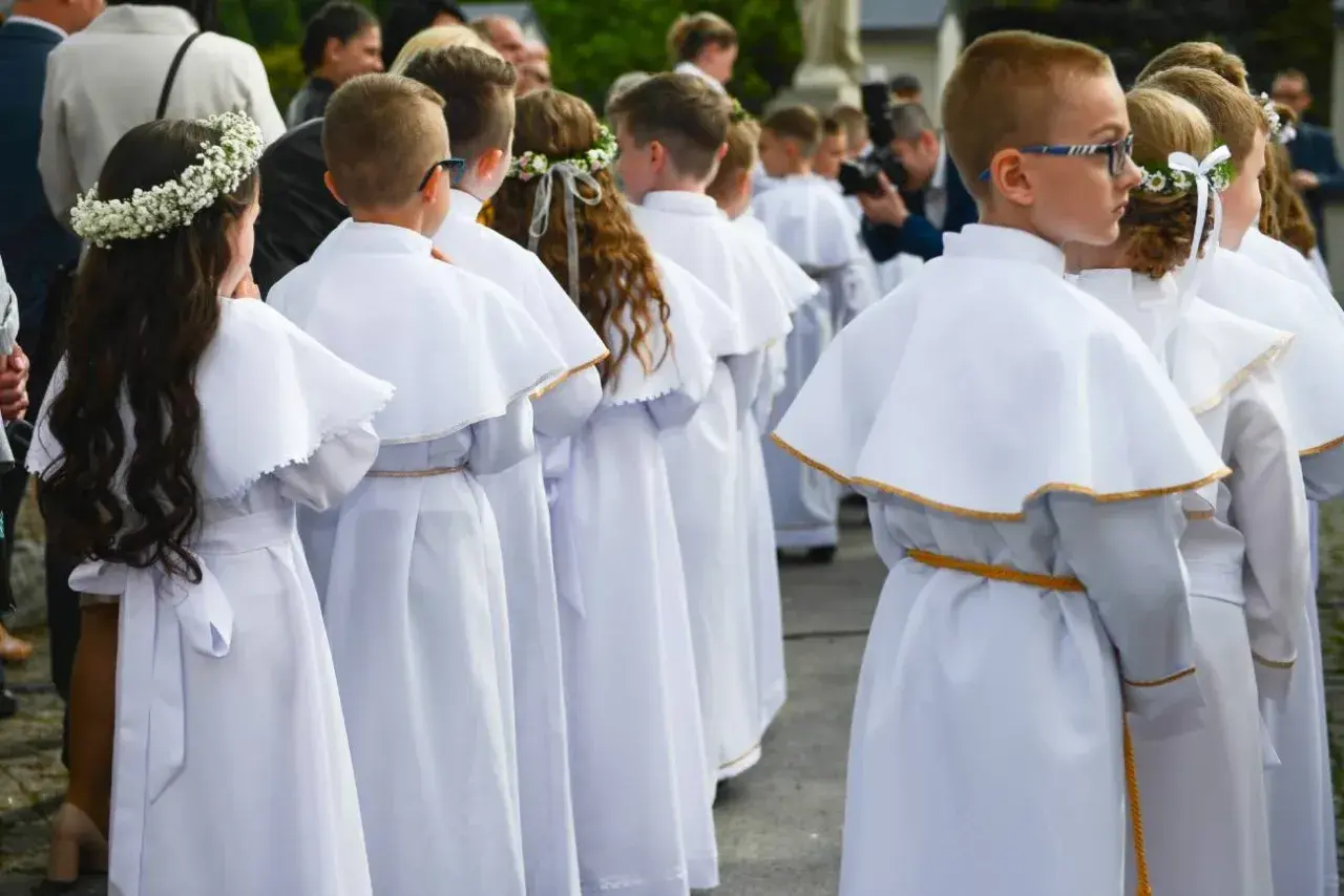 Dzieci w białych strojach komunijnych, dziewczynka z wiankiem na głowie. Piękne życzenia na komunie dla wszystkich.